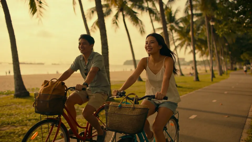 Friends cycling along a beachside park path under coconut palms in eastern Singapore, morning